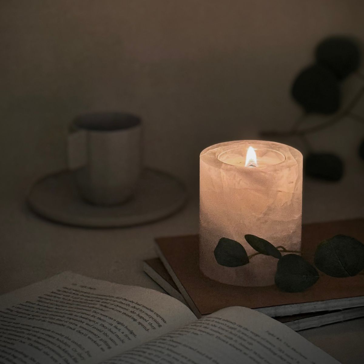 White crystal candle softly glowing in the dark, next to an open book and ceramic coffee cup—perfect for nighttime rituals.