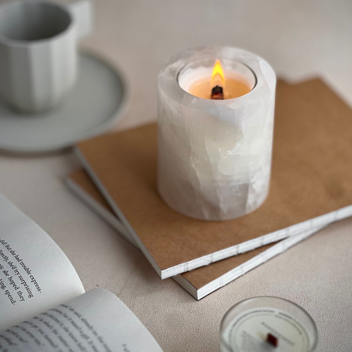 Minimalist crystal candleholder on stacked notebooks with a warm flame, styled for cozy home moments.